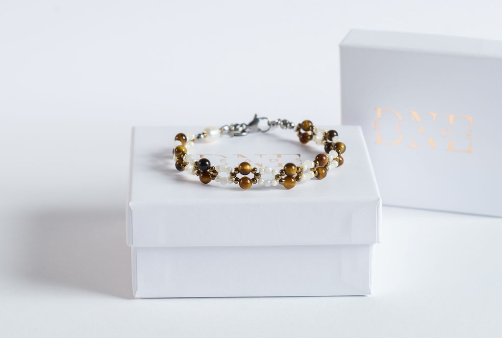 Das Twister-Armband Autumn Glow verbindet warm schimmerndes Tigerauge mit zarten Mondsteinperlen und feinen weißen sowie goldenen Glasperlen. Die gedrehte Struktur lässt die unterschiedlichen Steine wie einen weichen Farbverlauf ums Handgelenk fließen und fängt die Stimmung eines goldenen Herbsttages ein.