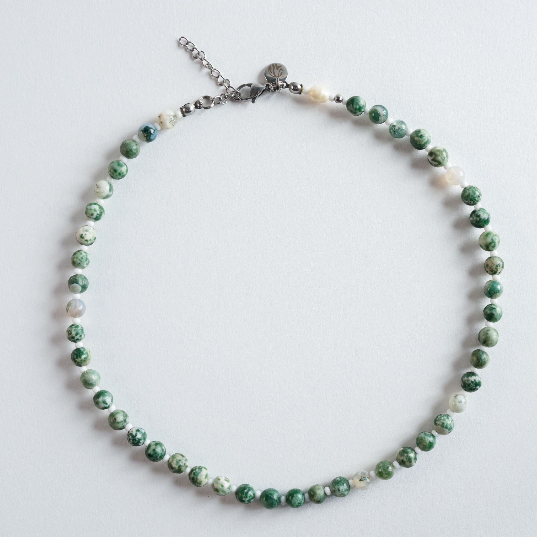„Forest Pearl“ kombiniert sanft gemaserten Baumachat mit feinen weißen Glasperlen. Die natürliche Grüntönung erinnert an Waldlicht und vermittelt Ruhe, Balance und Erdung. Eine harmonische, klare Kette, die Natürlichkeit und Minimalismus elegant verbindet.