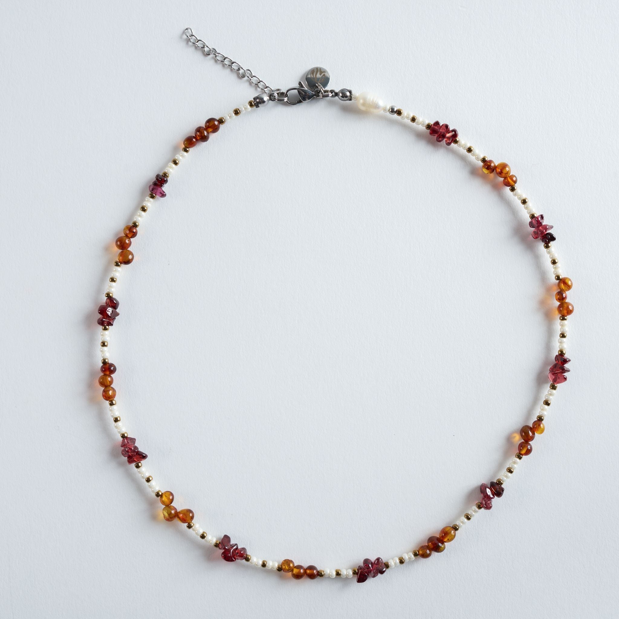 Die Kette „Amber Roots“ kombiniert warm schimmernden Bernstein mit tiefroten Granatsteinen und feinen, hellen Perlenakzenten.
