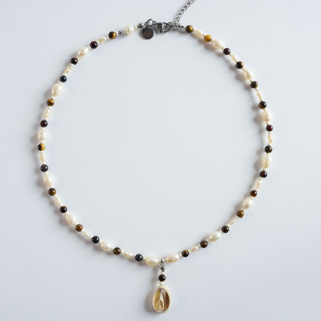 Die Halskette „Golden Coast“ kombiniert warm schimmerndes Tigerauge mit natürlichen Süßwasserperlen und einem Muschelanhänger.