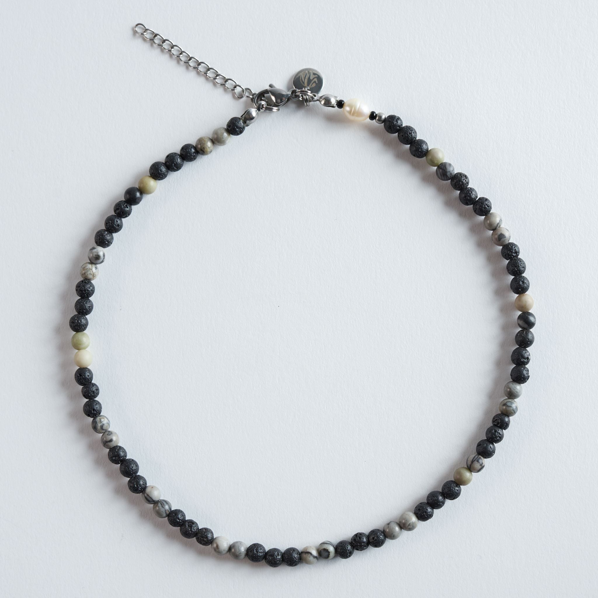 Die Kette „Grey Lava“ vereint die markante Textur von Lavastein mit sanft gemusterten Picture-Jasper-Perlen (Safari Jasper). Die Kombination aus tiefem Schwarz und natürlichen Grau-Beige-Schattierungen erzeugt einen ruhigen, minimalistischen Look. Ein dezentes, neutrales Design, das sich mit jedem Stil kombinieren lässt.
