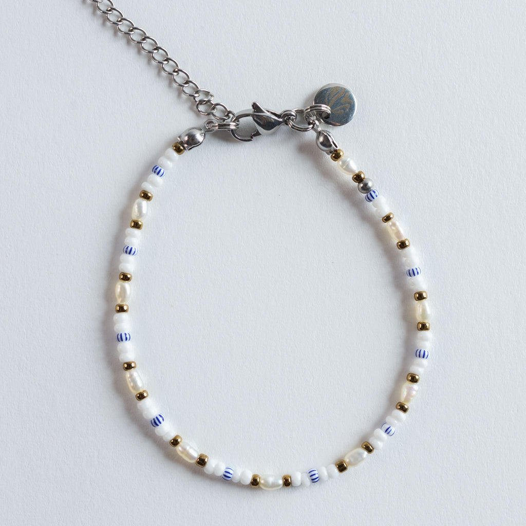 Das Armband „Mama Mia“ verbindet zarte Süßwasserperlen mit blau-weiß gestreiften Glasperlen und warmen Goldakzenten. Die maritime Farbwelt erinnert an Sommer, helles Sonnenlicht und das leichte Spiel von Wellen am Strand. Die Twister-Anordnung verleiht dem Design eine sanfte Bewegung, sodass ein frischer, lebendiger Rhythmus entsteht.
Ein moderner, verspielter Look, der Leichtigkeit und Sommerenergie vermittelt.