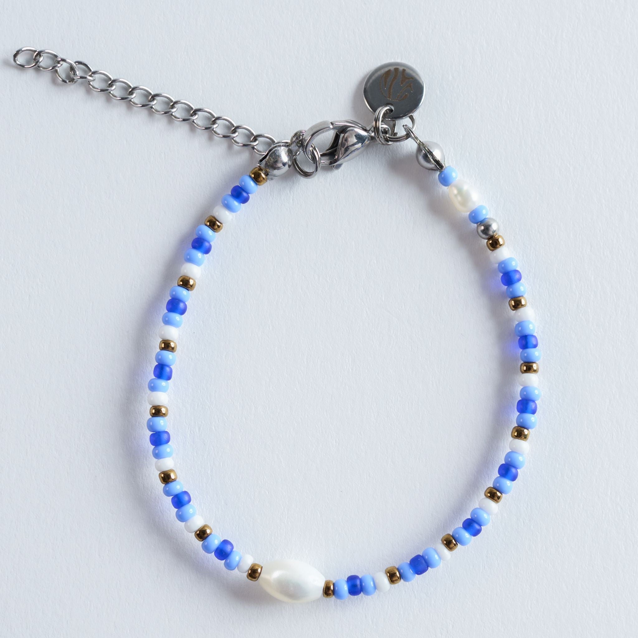 Das Armband Sky fängt die klare Leichtigkeit eines sonnigen Himmels über dem Meer ein. Verschiedene Blautöne greifen ineinander wie sanfte Wellen, unterbrochen von weißen Details und kleinen goldenen Lichtpunkten.