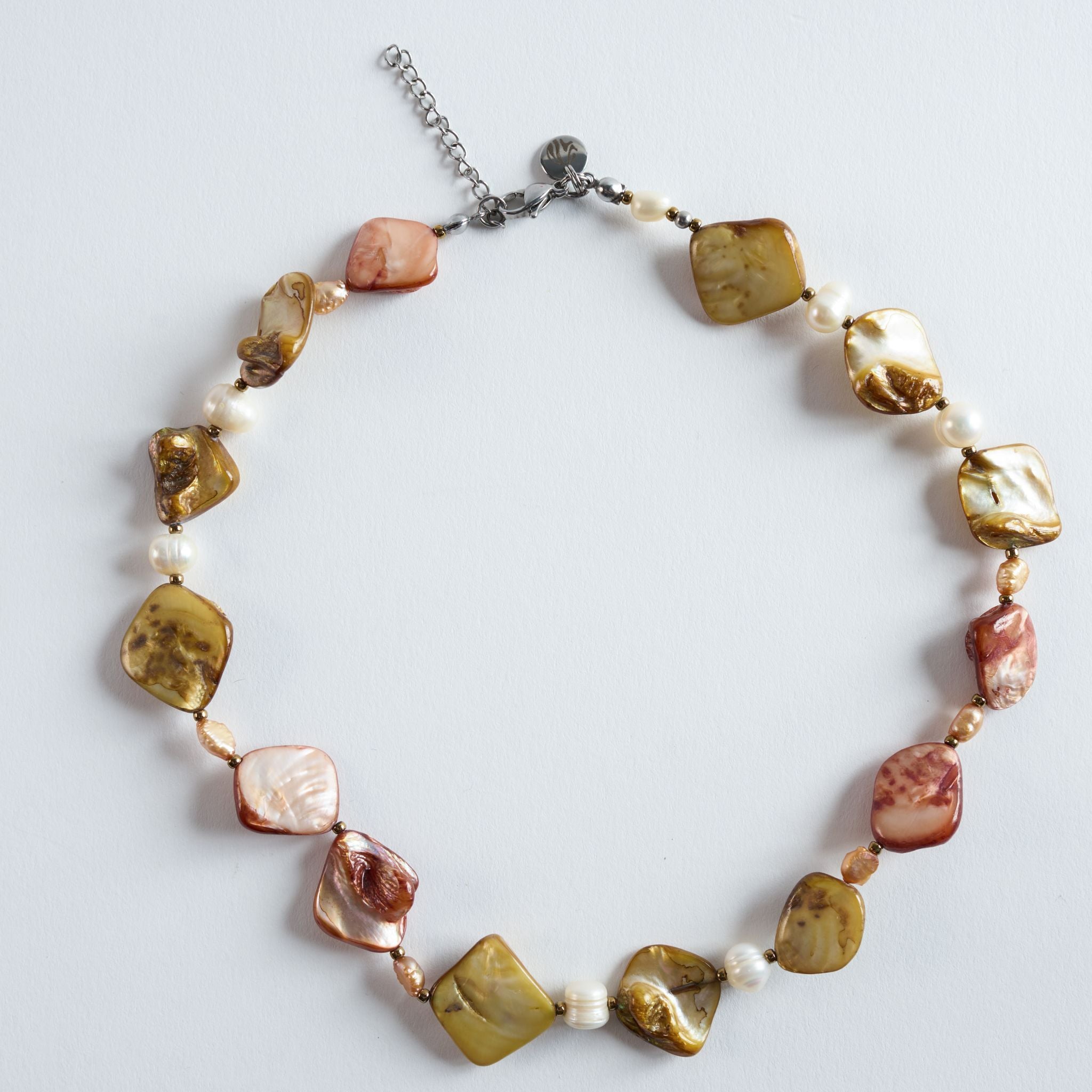 Die Halskette „Stingray“ kombiniert unregelmäßig geformte Perlmutt-Elemente in warmen Naturtönen mit hellen Süßwasserperlen und goldenen Details.