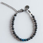 Das Armband Arctic Lava verbindet die natürliche, matte Struktur des Lavasteins mit den schimmernden Graunuancen von Labradorit und dem lebendigen Türkiston gefärbten Tigerauges. Die Mischung aus tiefem Schwarz, sanften Grautönen und klarem Türkis erinnert an kontrastreiche Landschaften, in denen vulkanisches Gestein auf eisige Küsten trifft.