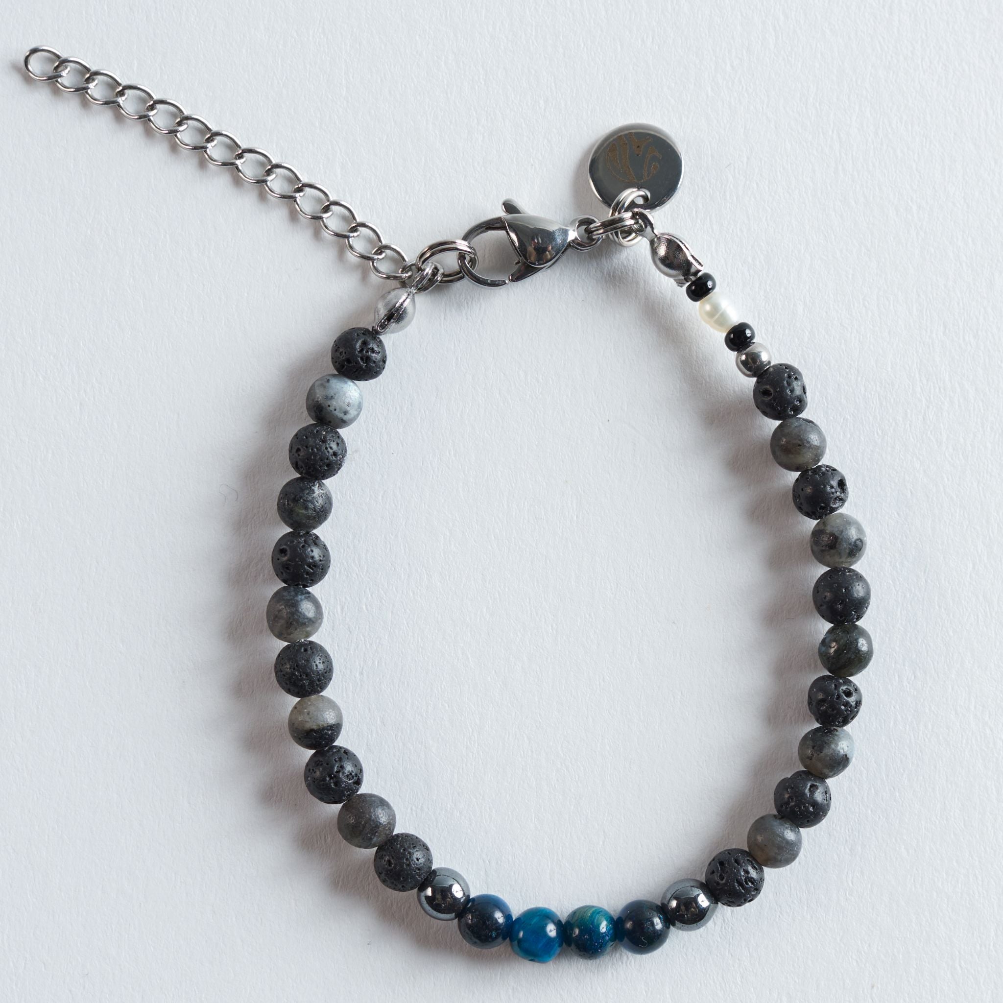 Das Armband Arctic Lava verbindet die natürliche, matte Struktur des Lavasteins mit den schimmernden Graunuancen von Labradorit und dem lebendigen Türkiston gefärbten Tigerauges. Die Mischung aus tiefem Schwarz, sanften Grautönen und klarem Türkis erinnert an kontrastreiche Landschaften, in denen vulkanisches Gestein auf eisige Küsten trifft.